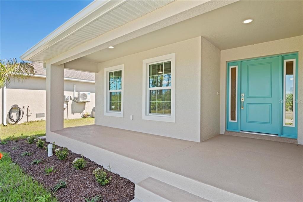 A covered front porch features a teal front door with sidelights and two windows — 109 BEAU RIVAGE DRIVE, ROTONDA WEST, FL