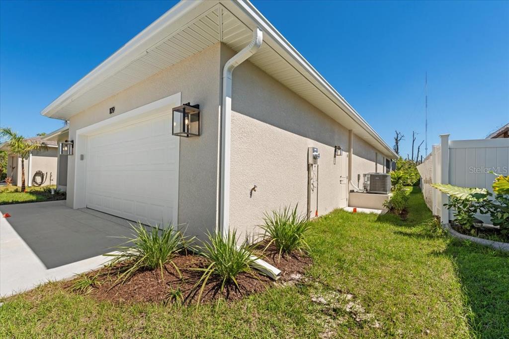 A side view of a beige house exterior featuring a garage, landscaping, and HVAC unit — 109 BEAU RIVAGE DRIVE, ROTONDA WEST, FL