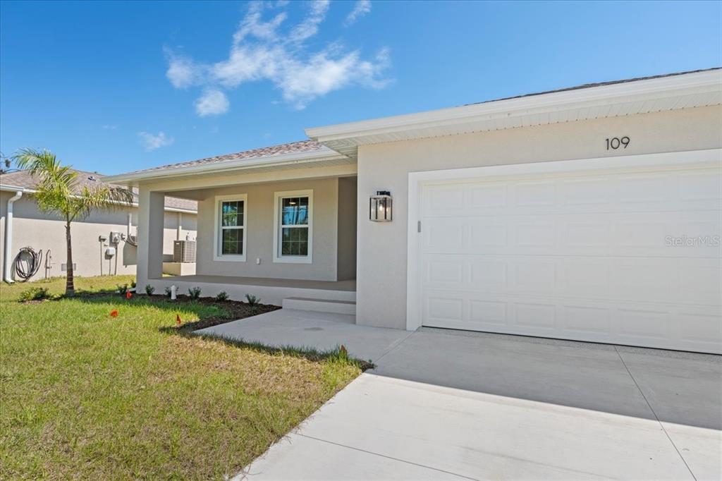 A light-colored single-story house exterior features a two-car garage, a covered porch, and landscaping — 109 BEAU RIVAGE DRIVE, ROTONDA WEST, FL
