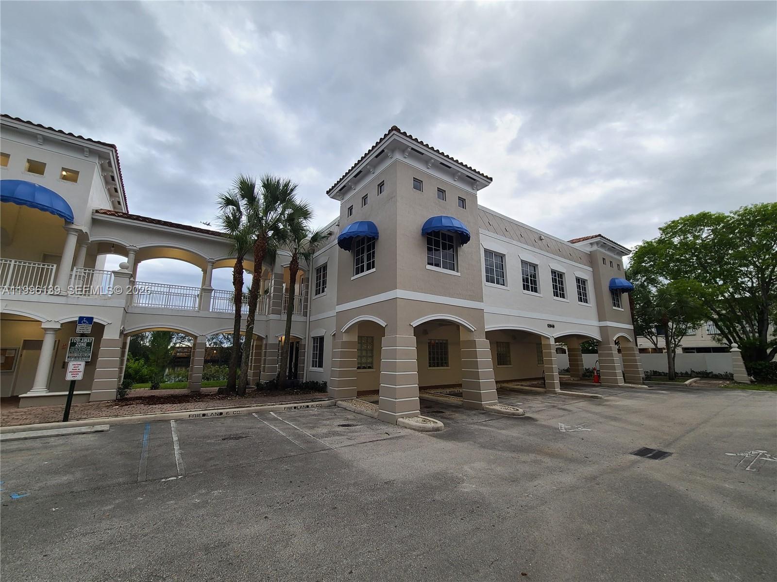 A two-story commercial building with arched walkways, blue awnings, and a paved parking lot — 12940 SW 128th St # 202, Miami FL 33186, MIAMI, FL