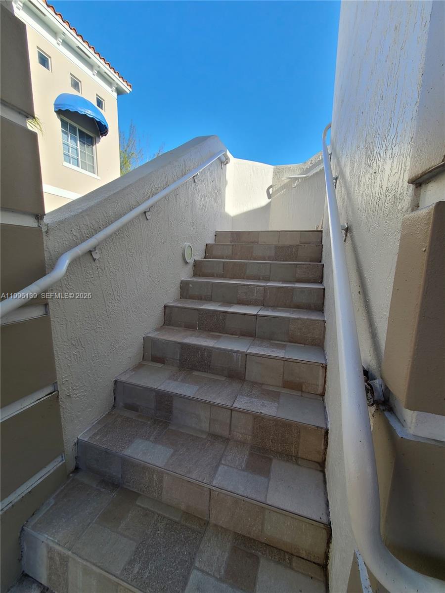 An outdoor staircase with tiled steps and white handrails leads up between two stucco walls — 12940 SW 128th St # 202, Miami FL 33186, MIAMI, FL