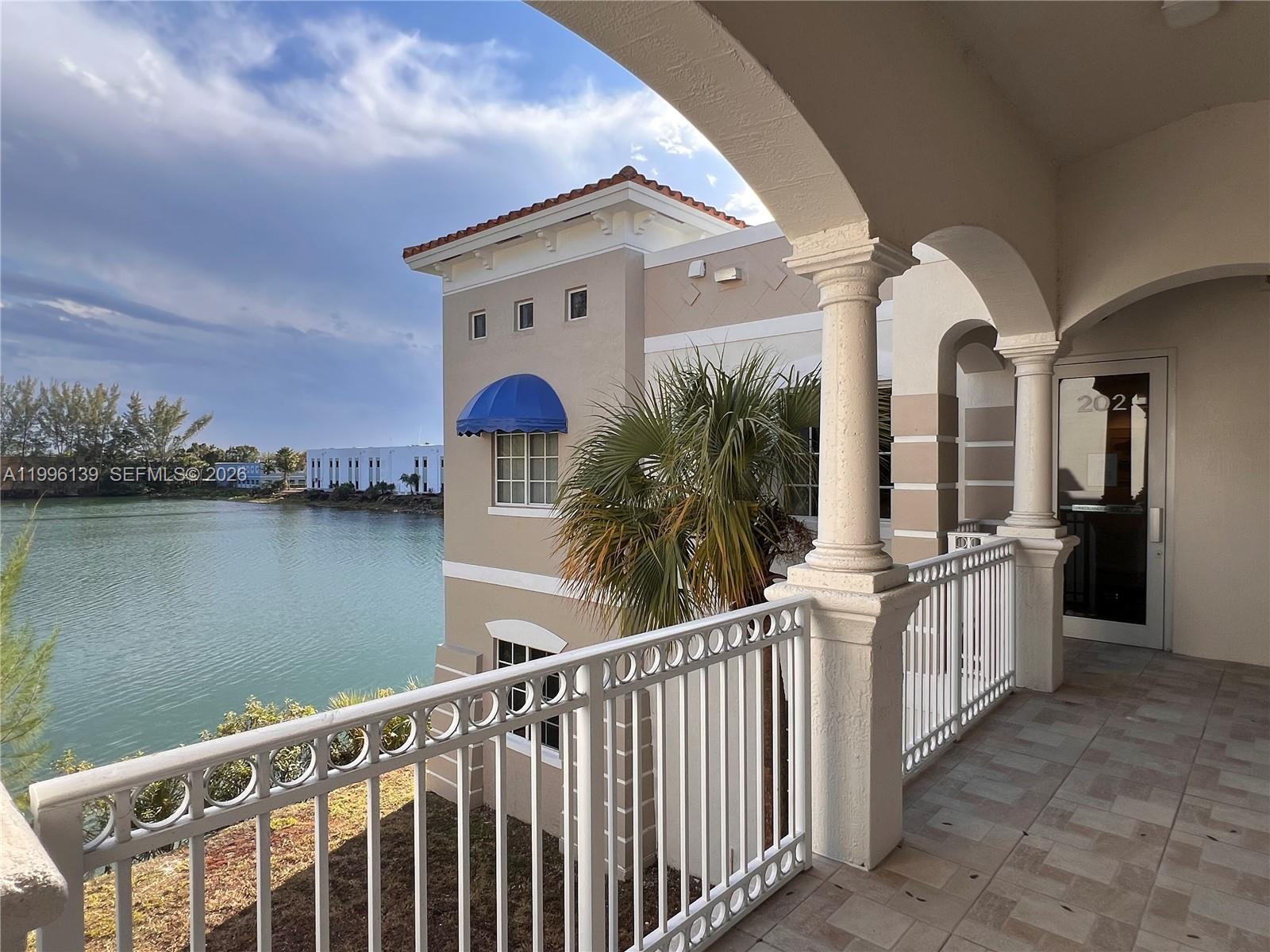 A balcony with a white metal railing overlooks a body of water and a building — 12940 SW 128th St # 202, Miami FL 33186, MIAMI, FL