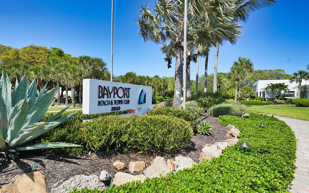 A white sign for Bayport Beach & Tennis Club stands in a landscaped garden area — 750 BAYPORT WAY UNIT 750, LONGBOAT KEY, FL