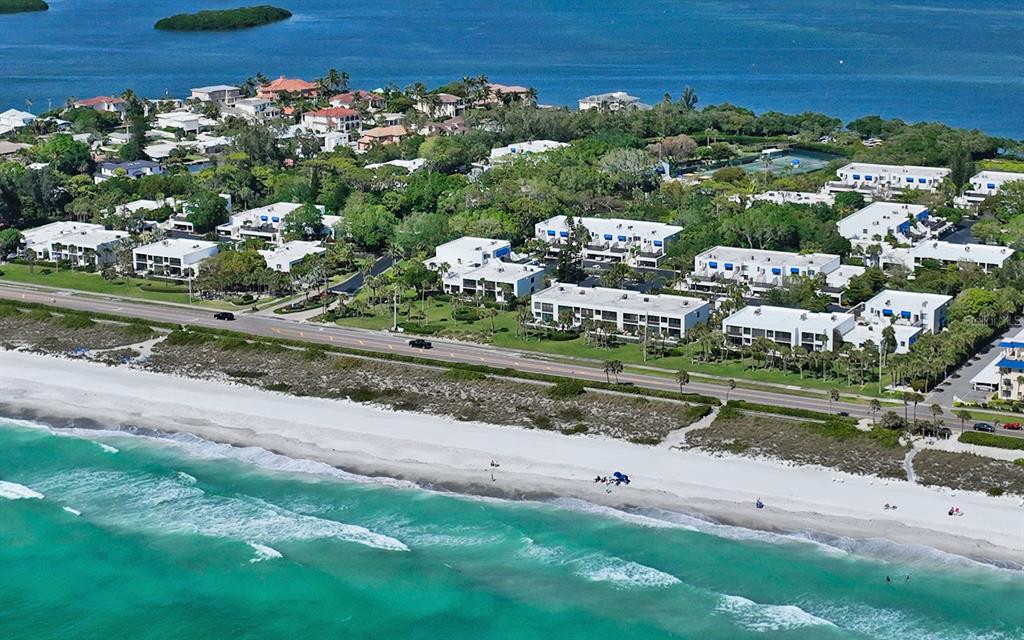 An aerial view shows a beach with turquoise water, a coastal road, and residential buildings — 750 BAYPORT WAY UNIT 750, LONGBOAT KEY, FL