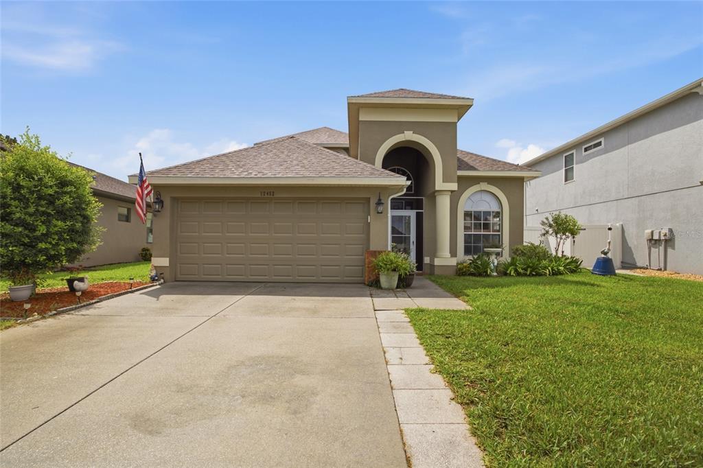 A single-story house with a tan stucco exterior, a two-car garage, and a paved driveway — 12452 CRICKLEWOOD DRIVE, SPRING HILL, FL