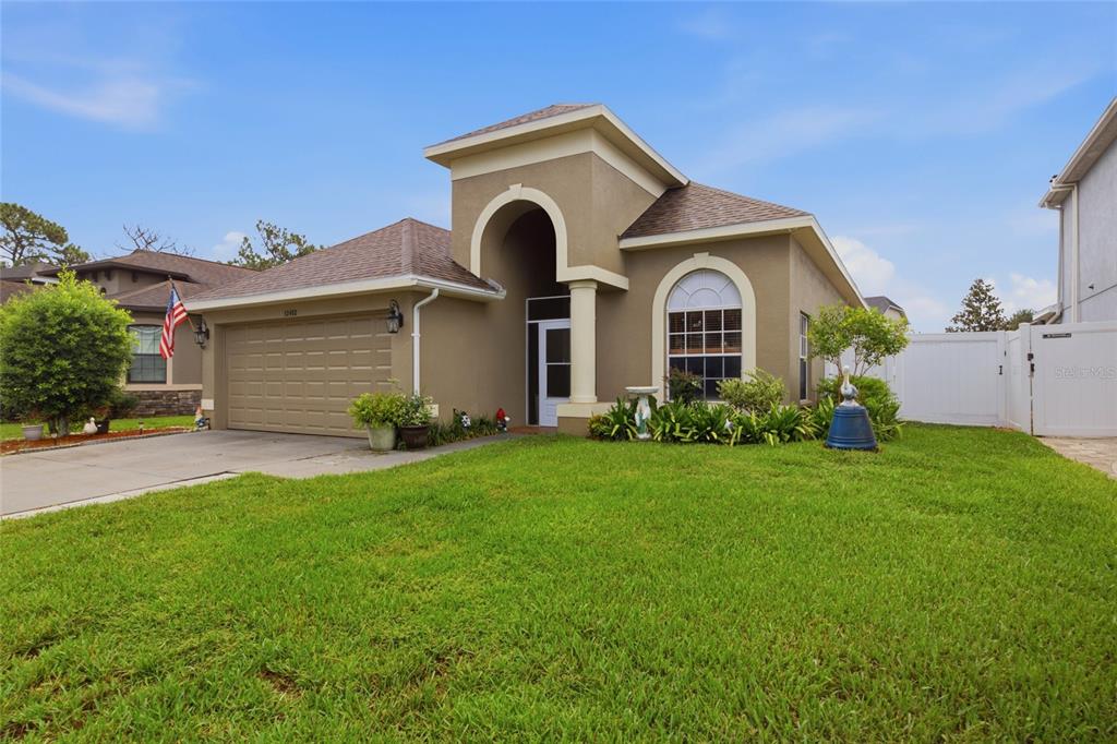 A single-story tan house with a two-car garage and a prominent arched entryway — 12452 CRICKLEWOOD DRIVE, SPRING HILL, FL