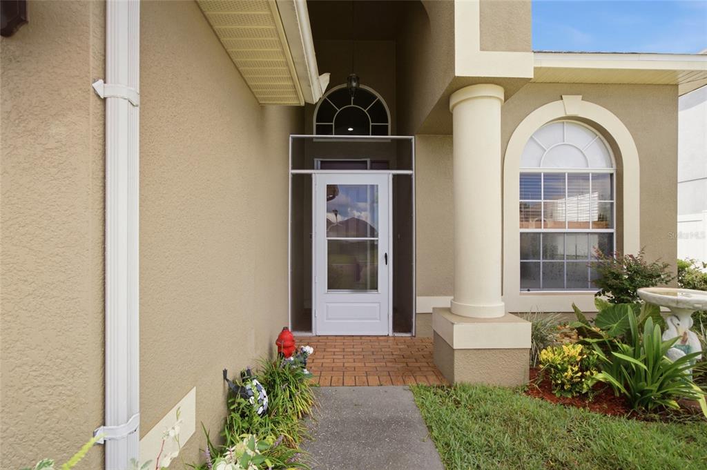 The exterior entrance features a white storm door, a column, and a brick walkway — 12452 CRICKLEWOOD DRIVE, SPRING HILL, FL