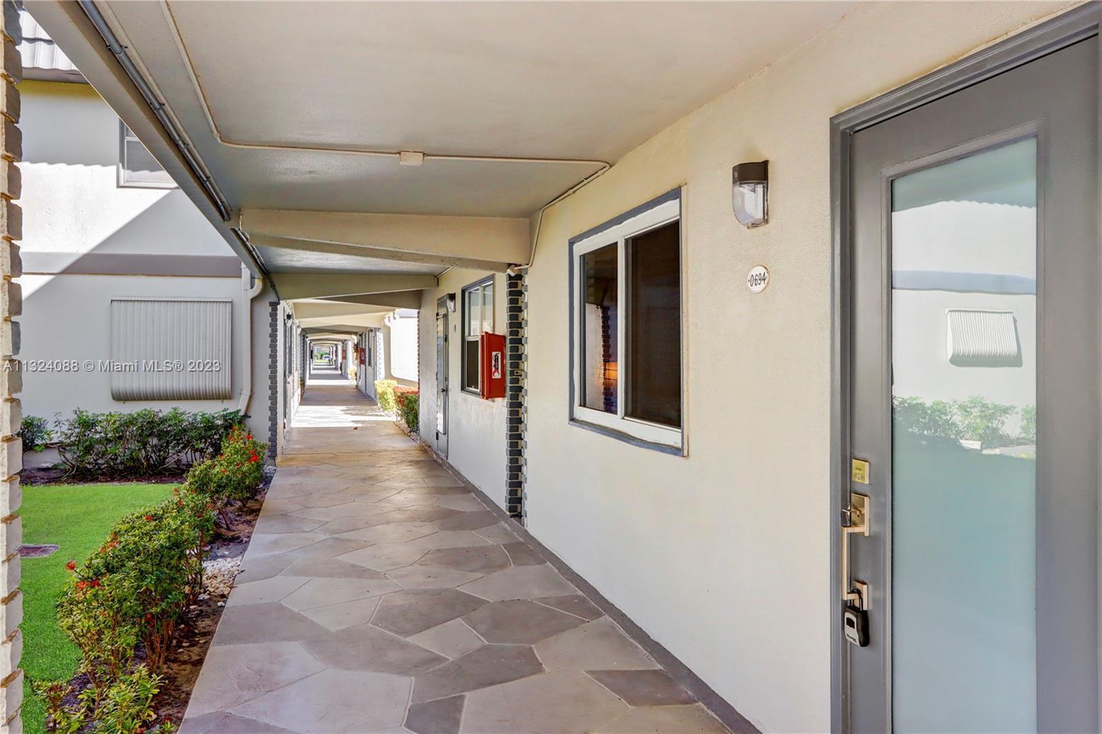 A covered outdoor walkway leads past a gray door and a window with a fire extinguisher — 694 Brittany Park # O, Delray Beach FL 33446, DELRAY BEACH, FL