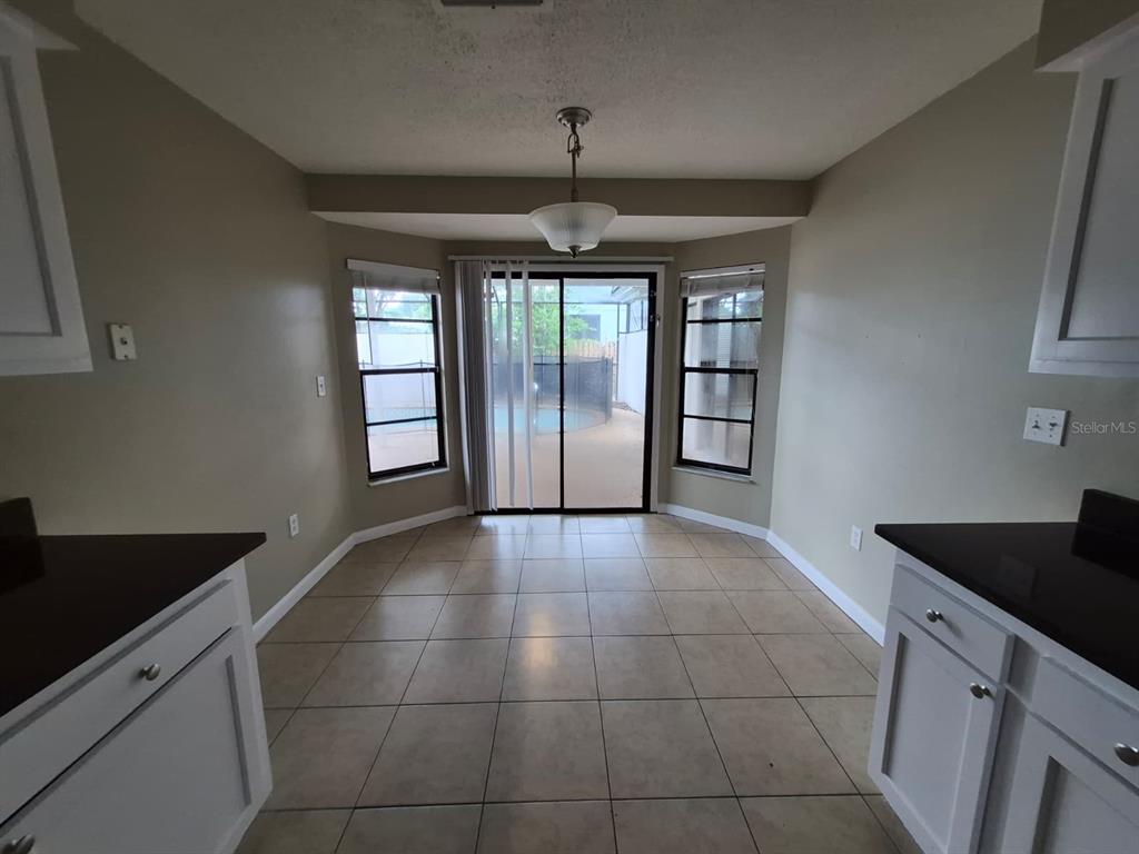 A galley kitchen features white cabinets, black countertops, and light-colored tile flooring — 10227 LANDMARK DRIVE, HUDSON, FL