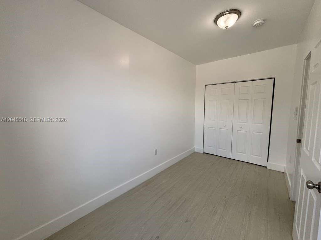An empty bedroom features white walls, light wood-look flooring, and a white bi-fold closet door — 1051 NW 2nd St # 10, Miami FL 33128, MIAMI, FL