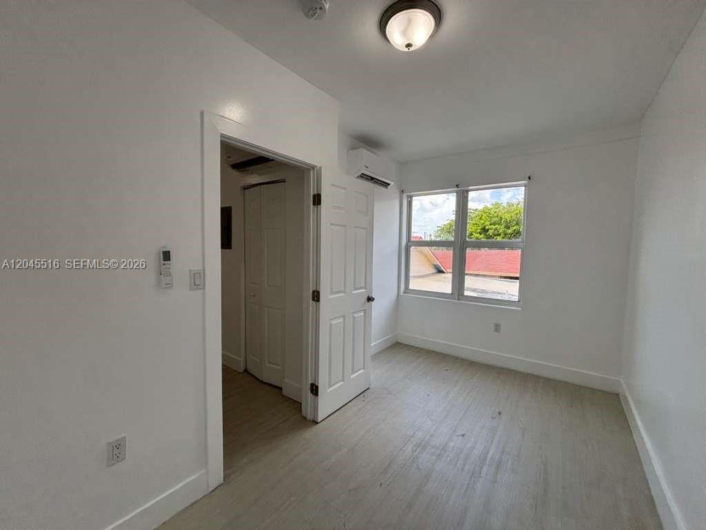 A bedroom with light-colored flooring, a white door, a window, and a wall-mounted air conditioner — 1051 NW 2nd St # 10, Miami FL 33128, MIAMI, FL