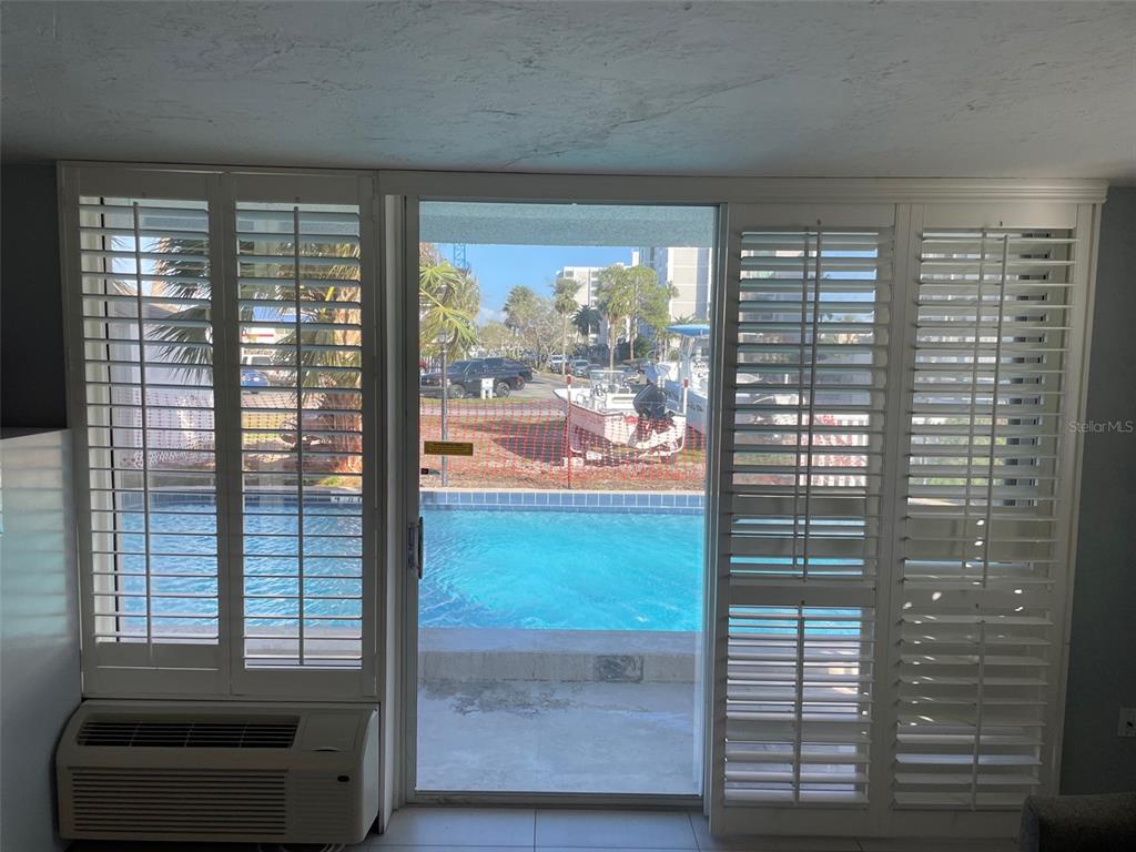 A room with white plantation shutters overlooks a swimming pool and a boat parked outside — 800 BAYWAY BOULEVARD UNIT 14, CLEARWATER BEACH, FL