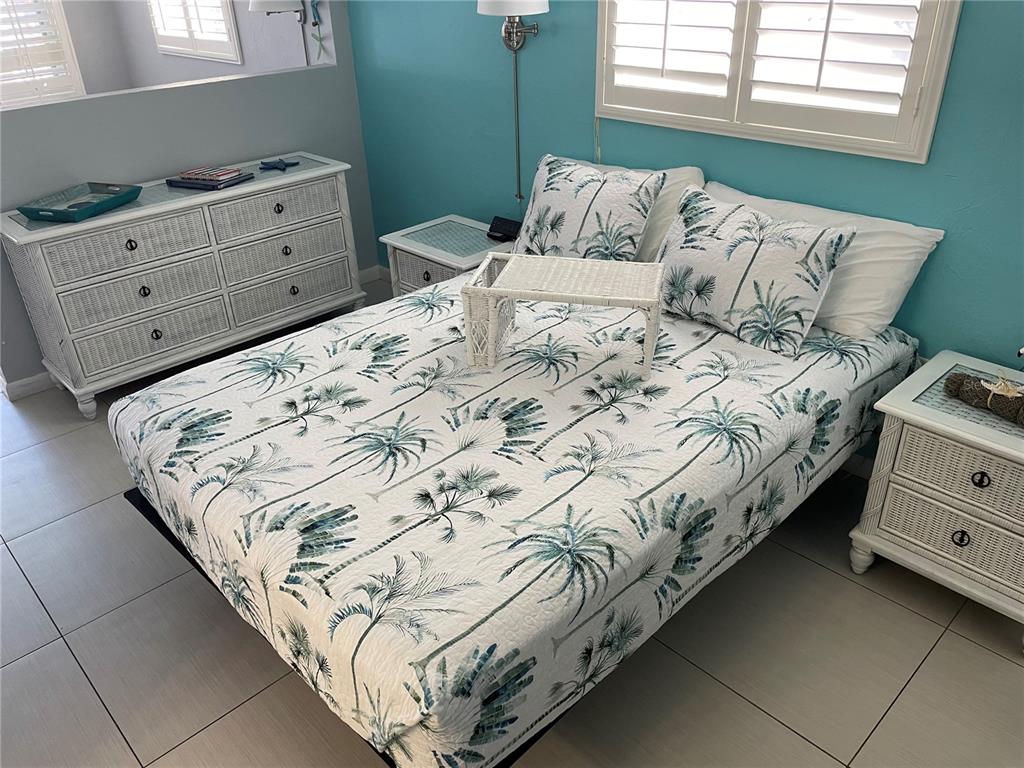 A bedroom features a bed with palm-print bedding, white wicker furniture, and light blue walls — 800 BAYWAY BOULEVARD UNIT 14, CLEARWATER BEACH, FL