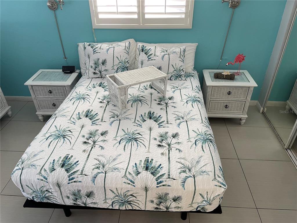 A bedroom features a bed with a palm tree print quilt, two white wicker nightstands, and teal walls — 800 BAYWAY BOULEVARD UNIT 14, CLEARWATER BEACH, FL