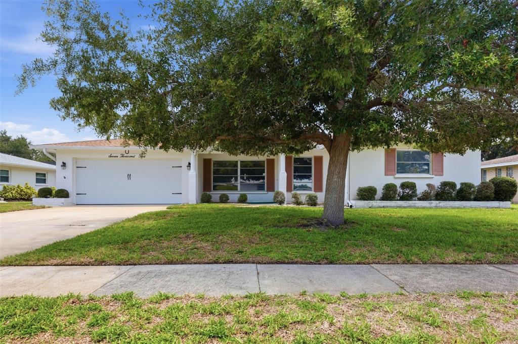 A single-story white house with a two-car garage, brown shutters, and a large front tree — 7005 ANTIGUA PLACE, SARASOTA, FL