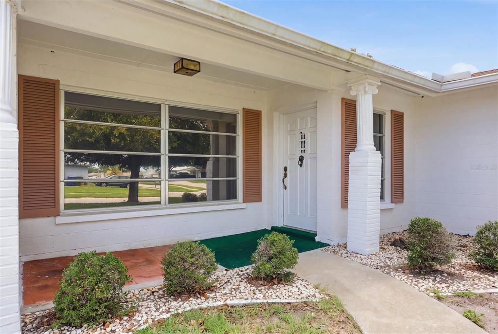 The exterior of a white house features a front door, a large window, and shutters — 7005 ANTIGUA PLACE, SARASOTA, FL