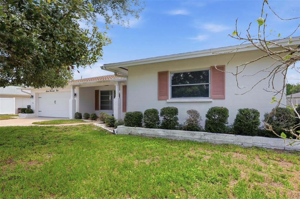 A white single-story house with a garage, pink shutters, and a front garden bed — 7005 ANTIGUA PLACE, SARASOTA, FL