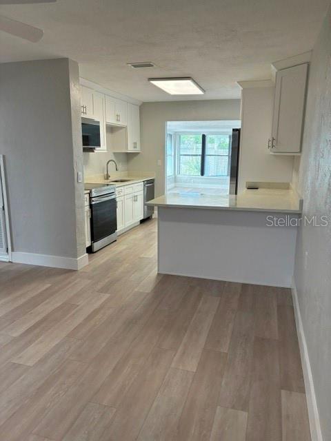 A kitchen features white cabinets, stainless steel appliances, and light wood-look flooring — 28 AZALEA DRIVE, ORMOND BEACH, FL