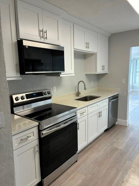 A modern kitchen features white cabinetry, stainless steel appliances, and light wood-look flooring — 28 AZALEA DRIVE, ORMOND BEACH, FL