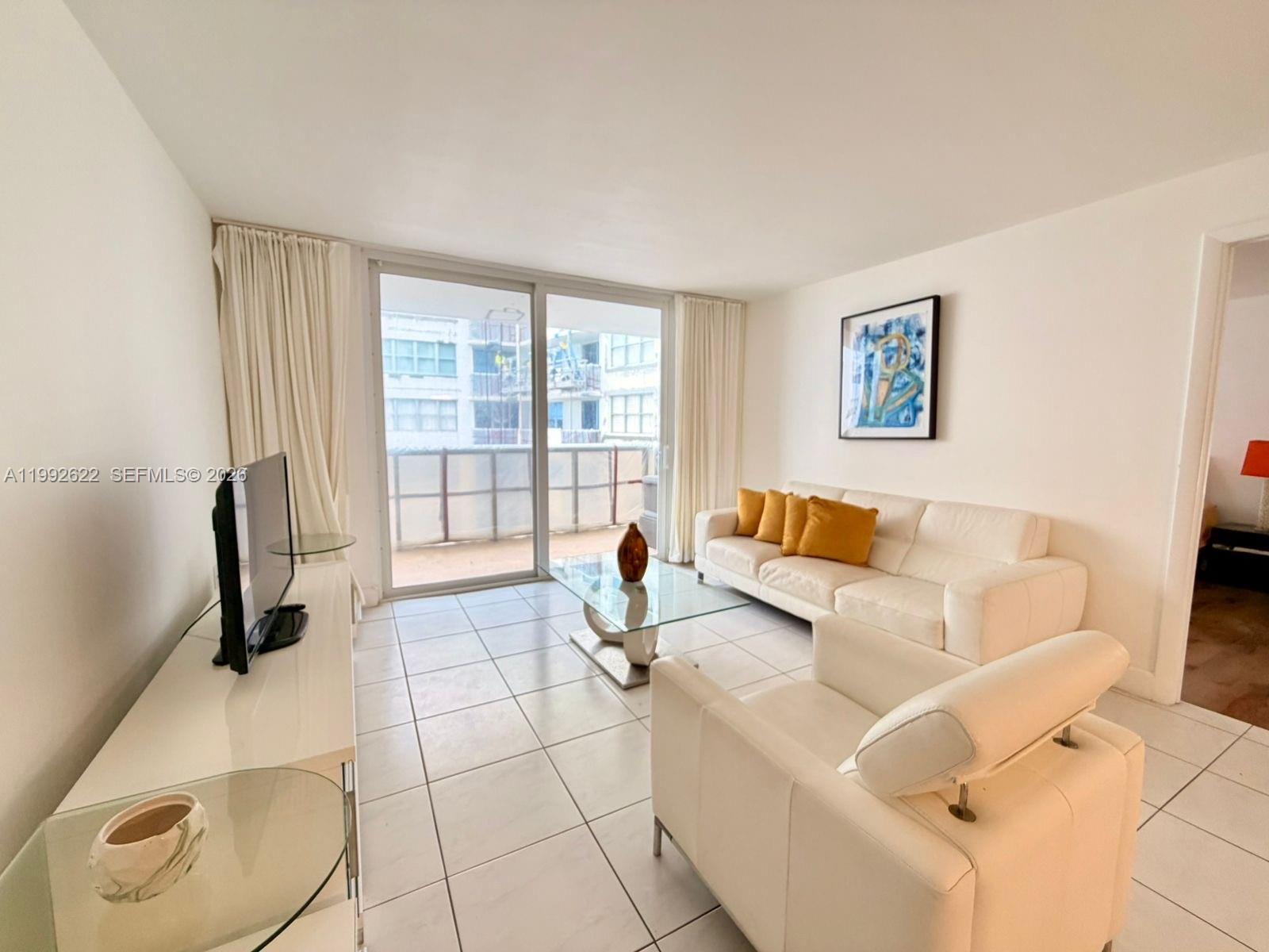 A living room features white tile floors, a white sofa with yellow pillows, and a balcony — 6039 Collins Ave # 1506, Miami Beach FL 33140, MIAMI BEACH, FL