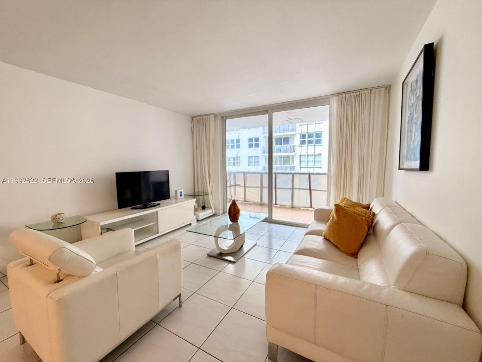A living room features white tile floors, a white sofa, and a glass coffee table — 6039 Collins Ave # 1506, Miami Beach FL 33140, MIAMI BEACH, FL