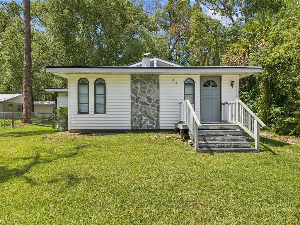 A single-story house with white siding, a stone chimney, and a wooden front porch — 111 E EARLY STREET, BROOKSVILLE, FL