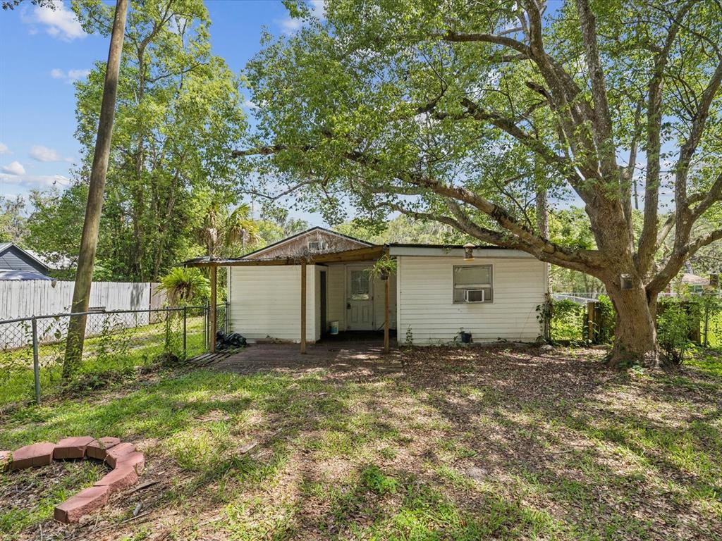 A small, white, single-story house with a covered porch sits in a tree-shaded backyard — 111 E EARLY STREET, BROOKSVILLE, FL