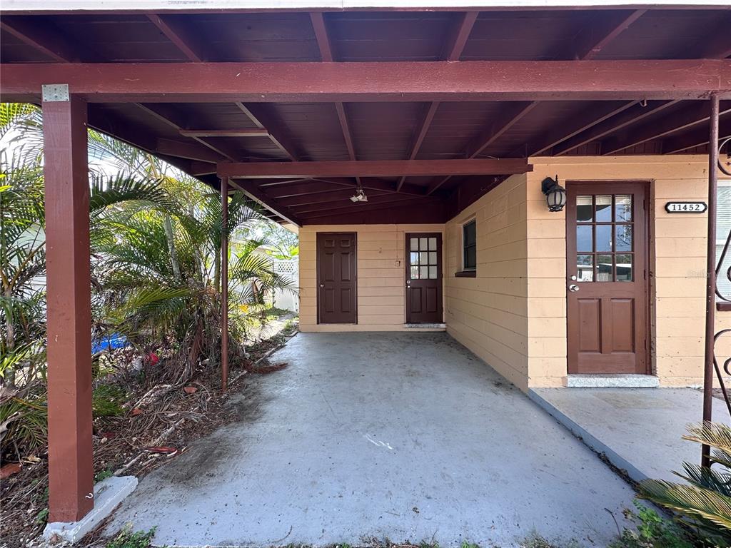 A covered carport area features a concrete floor and three brown doors on the exterior — 11452 104TH STREET, LARGO, FL