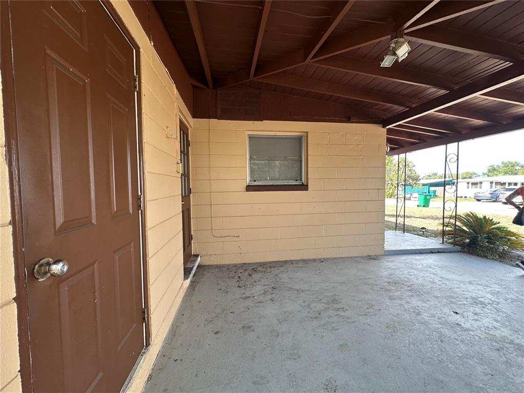 A covered concrete patio features a brown door and a window on a block wall — 11452 104TH STREET, LARGO, FL