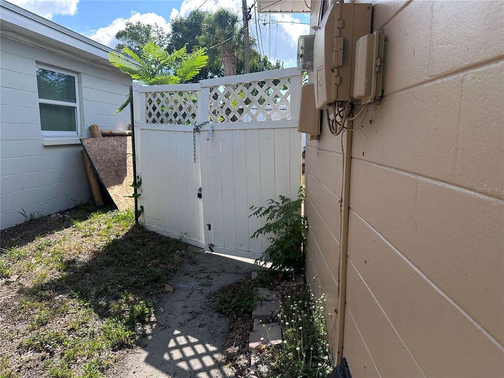 A white vinyl gate stands between a light-colored house and a tan exterior wall — 11452 104TH STREET, LARGO, FL