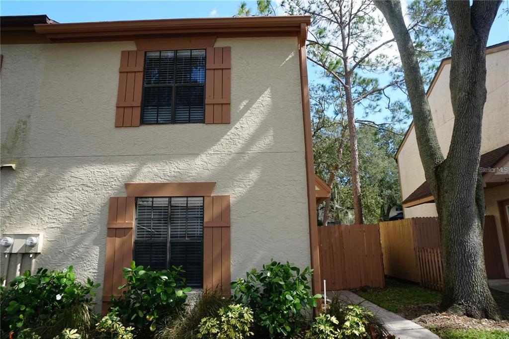 A two-story tan stucco townhouse with brown shutters and a wooden fence — 2404 BRIGADOON DRIVE, CLEARWATER, FL