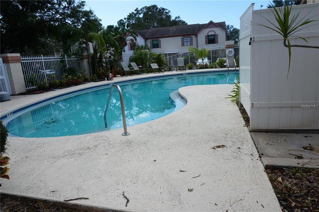 A swimming pool with a metal handrail sits beside a white fence and apartment building — 2404 BRIGADOON DRIVE, CLEARWATER, FL