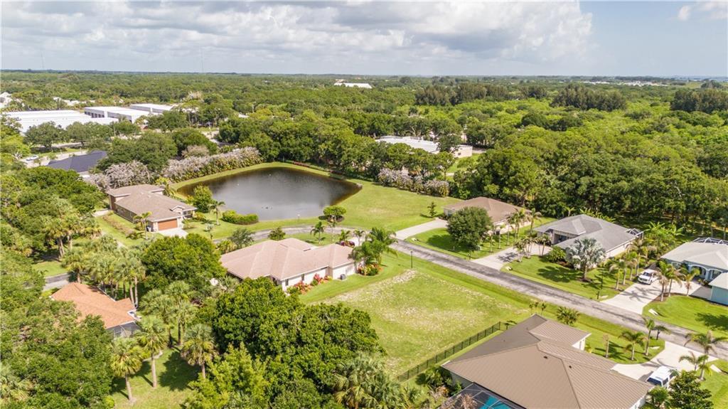 An aerial view shows several suburban houses, a small pond, and lush green trees — VERO BEACH, FL