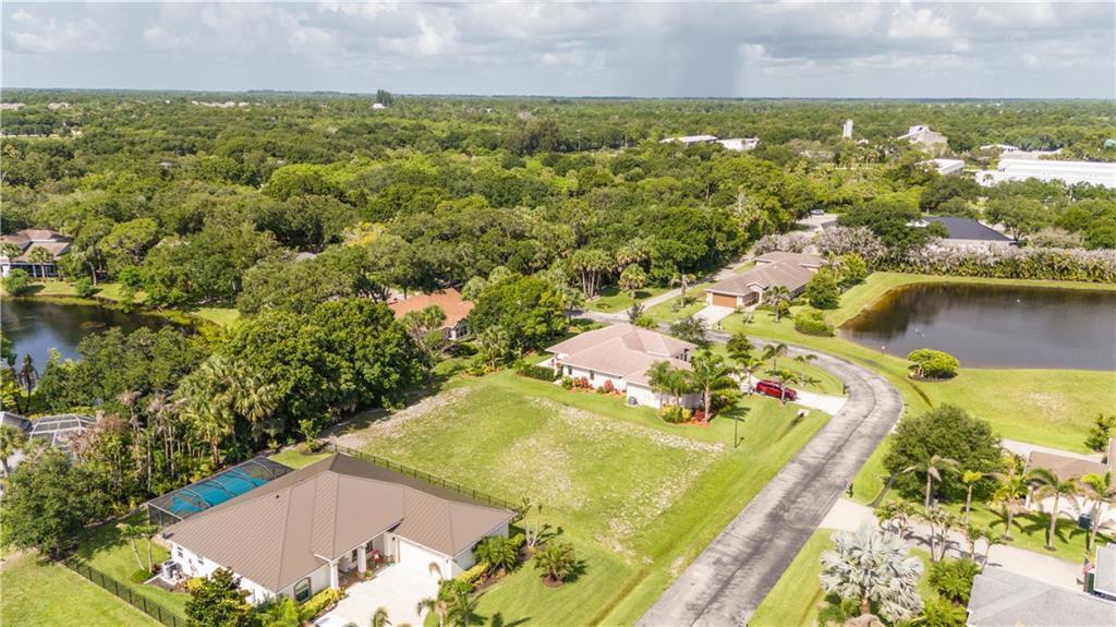 An aerial view shows several single-family homes with pools and ponds in a wooded neighborhood — VERO BEACH, FL