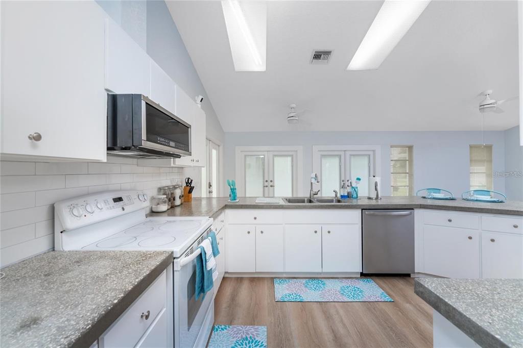 A kitchen features white cabinets, gray countertops, stainless steel appliances, and light wood-look flooring — 7456 JENNIFER DRIVE, PORT CHARLOTTE, FL