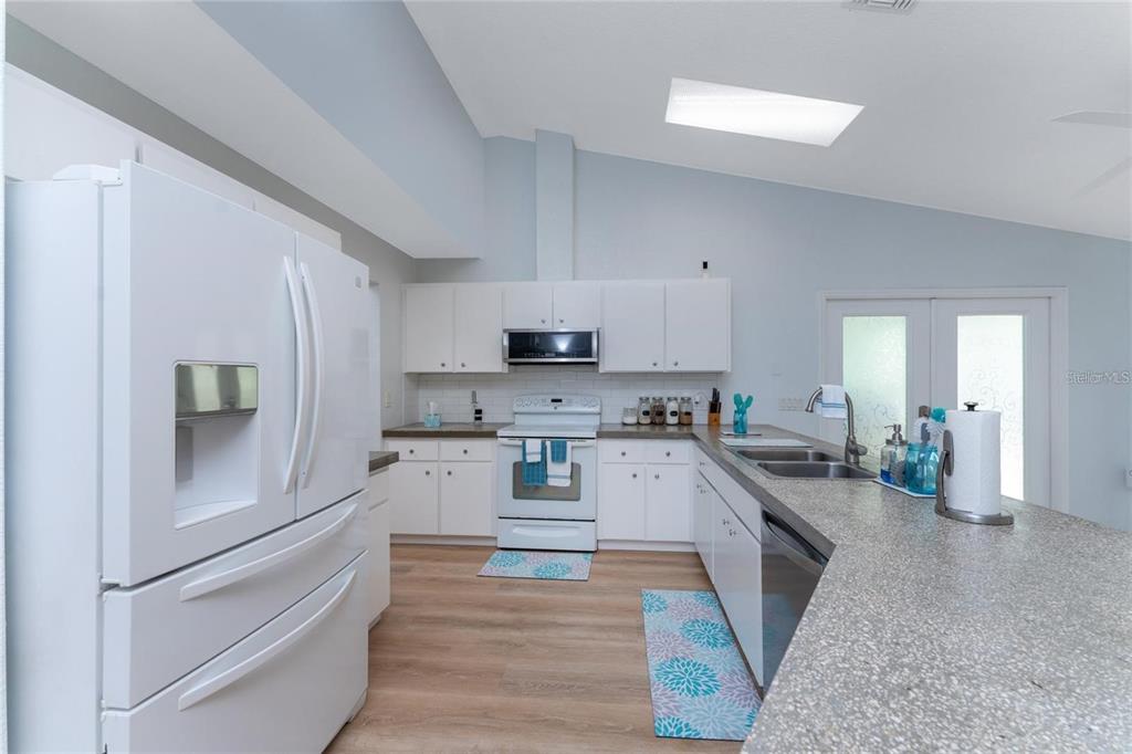 A kitchen features white cabinets, white appliances, a granite countertop, and light wood-look flooring — 7456 JENNIFER DRIVE, PORT CHARLOTTE, FL