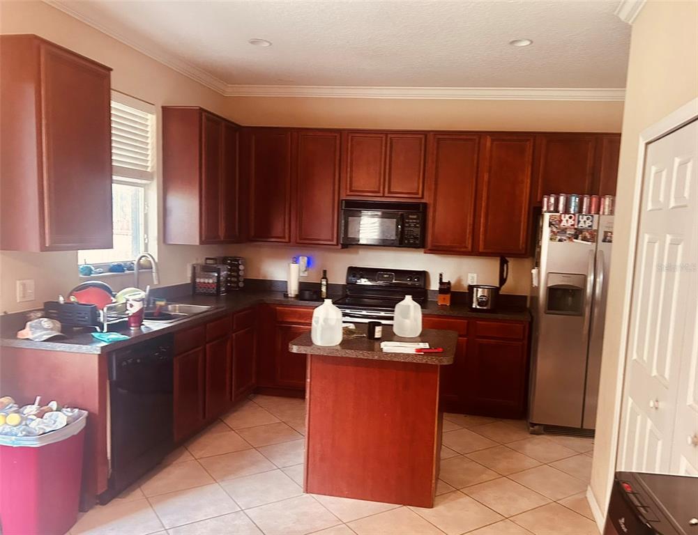 A kitchen features dark wood cabinets, a central island, stainless steel appliances, and tile flooring — 9962 BENNINGTON CHASE DRIVE, ORLANDO, FL