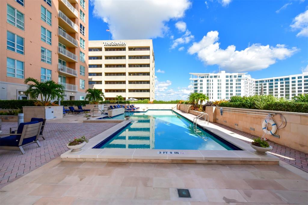 An outdoor swimming pool with a depth marker sits on a patio near tall buildings — 1350 MAIN STREET UNIT 908, SARASOTA, FL