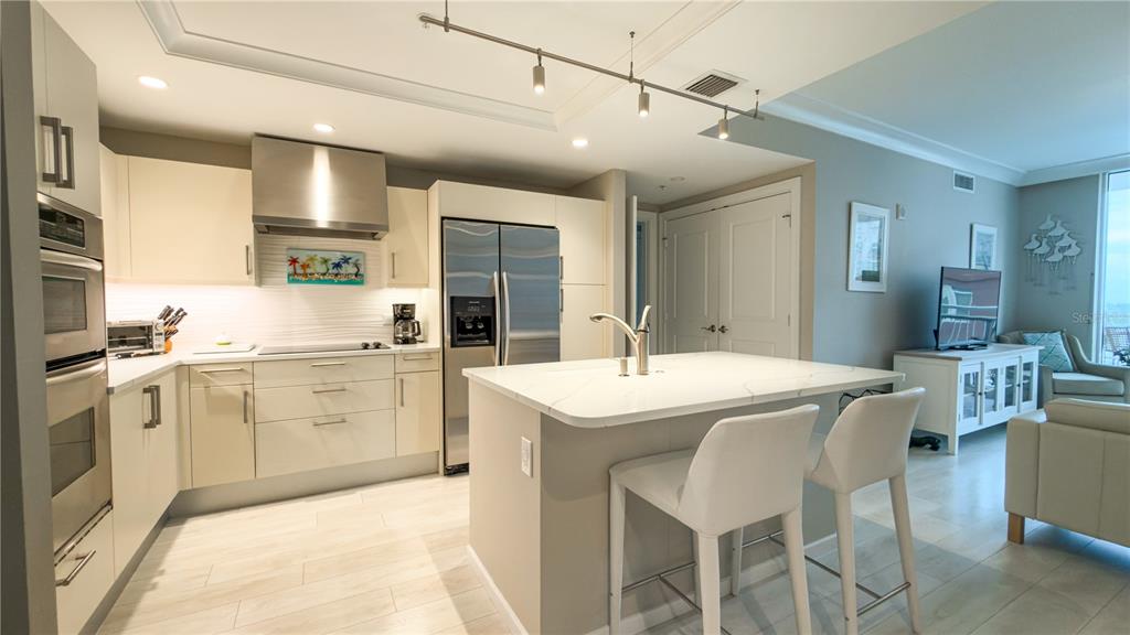 A modern kitchen features white cabinetry, stainless steel appliances, a center island, and bar seating — 1350 MAIN STREET UNIT 908, SARASOTA, FL