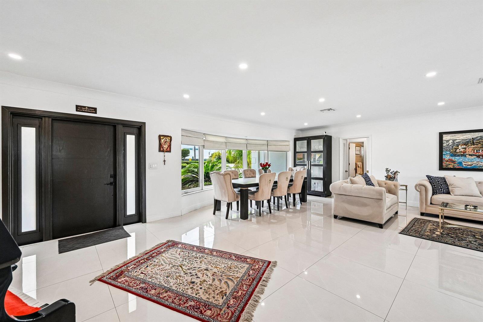 A bright, open-concept living and dining area features white tile floors and a dark front door — 2940 NE 39th Court, Lighthouse Point FL 33064, LIGHTHOUSE POINT, FL