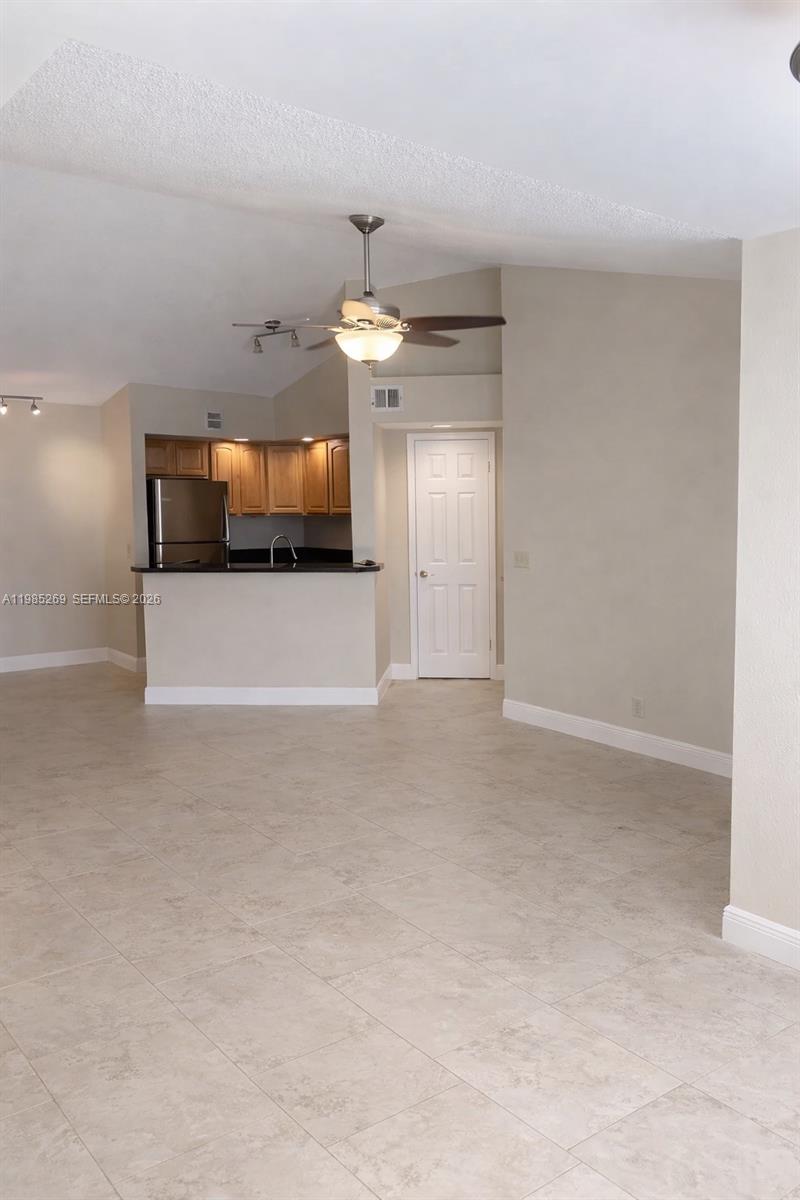 A living area with tile flooring leads to an open kitchen with wooden cabinets — 3410 N Pinewalk Dr N # 827, Margate FL 33063, MARGATE, FL