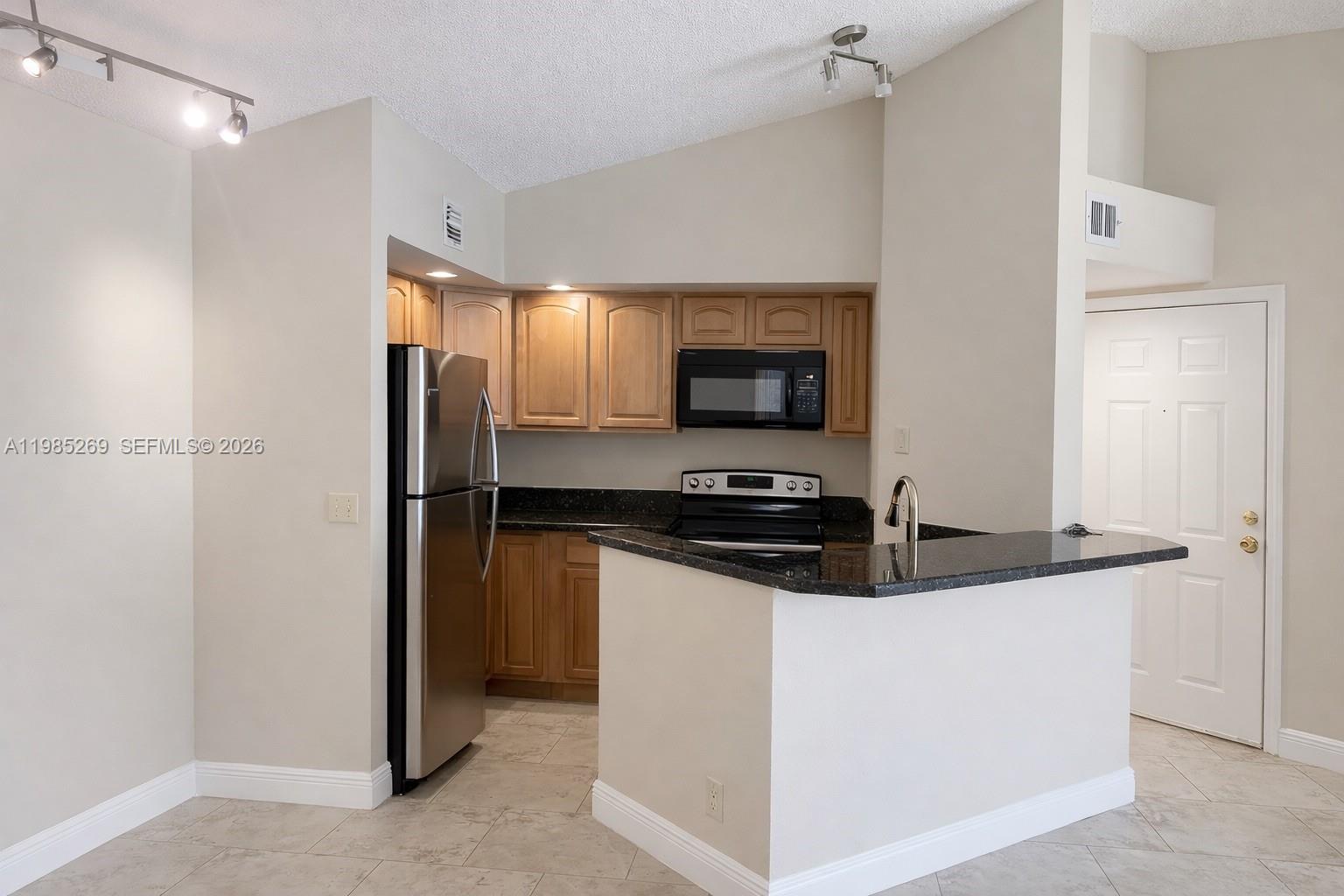 A kitchen features light wood cabinets, dark granite countertops, stainless steel appliances, and tile flooring — 3410 N Pinewalk Dr N # 827, Margate FL 33063, MARGATE, FL