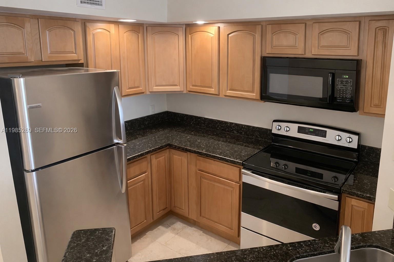 A kitchen features light wood cabinets, dark granite countertops, and stainless steel appliances — 3410 N Pinewalk Dr N # 827, Margate FL 33063, MARGATE, FL