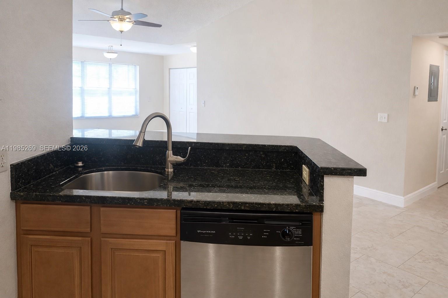 A kitchen sink and dishwasher are set into a dark granite countertop with wood cabinets — 3410 N Pinewalk Dr N # 827, Margate FL 33063, MARGATE, FL