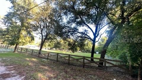 A wooden split-rail fence borders a grassy yard shaded by several large trees — 7678 SW 151ST PLACE, DUNNELLON, FL