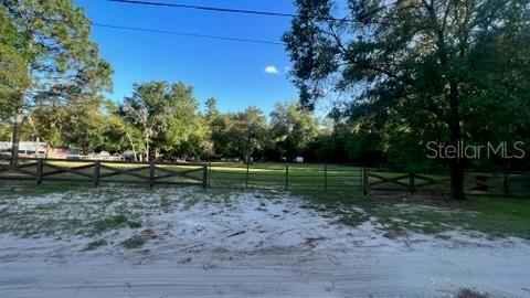 A fenced, grassy lot with mature trees sits behind a sandy foreground area — 7678 SW 151ST PLACE, DUNNELLON, FL