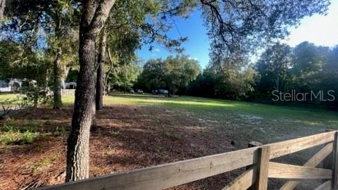 A wooden fence borders a grassy, tree-lined lot under a clear blue sky — 7678 SW 151ST PLACE, DUNNELLON, FL