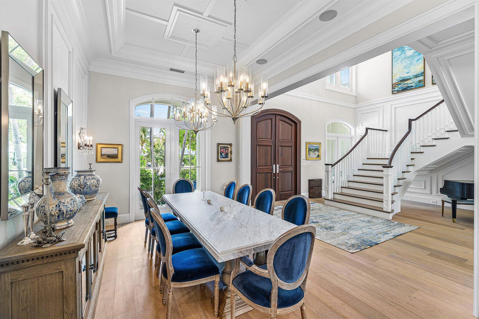 A dining room features a marble table, blue velvet chairs, chandeliers, and a grand staircase — 2249 E Maya Palm Drive, Boca Raton FL 33432, BOCA RATON, FL