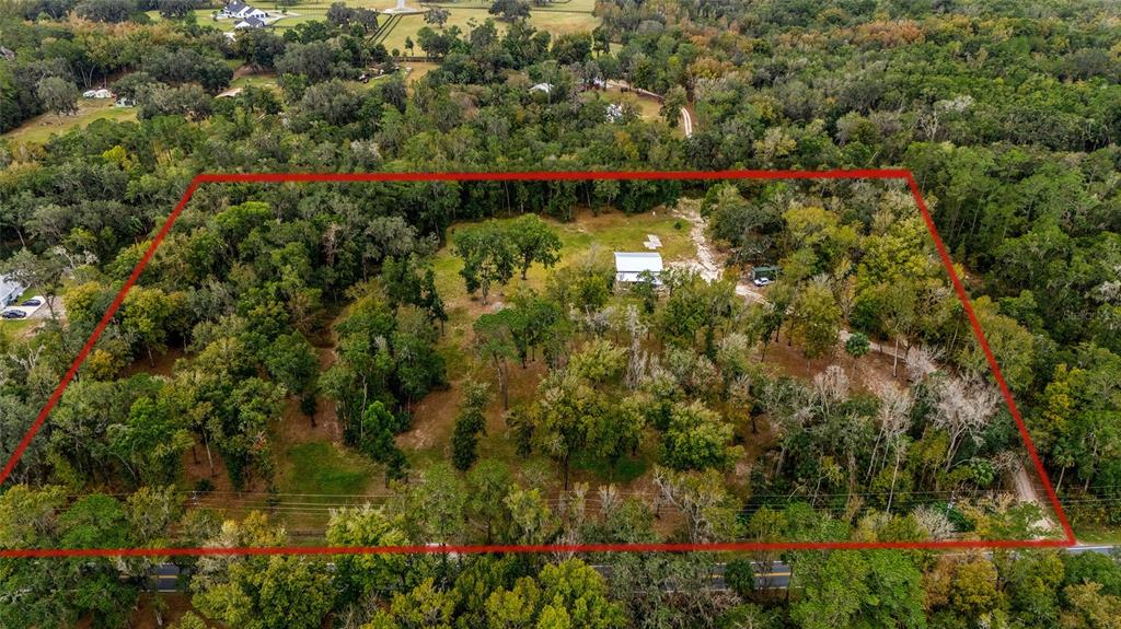A dirt driveway leads to a metal gate flanked by wooden fences and retaining walls — 2578 SE 110TH STREET, OCALA, FL