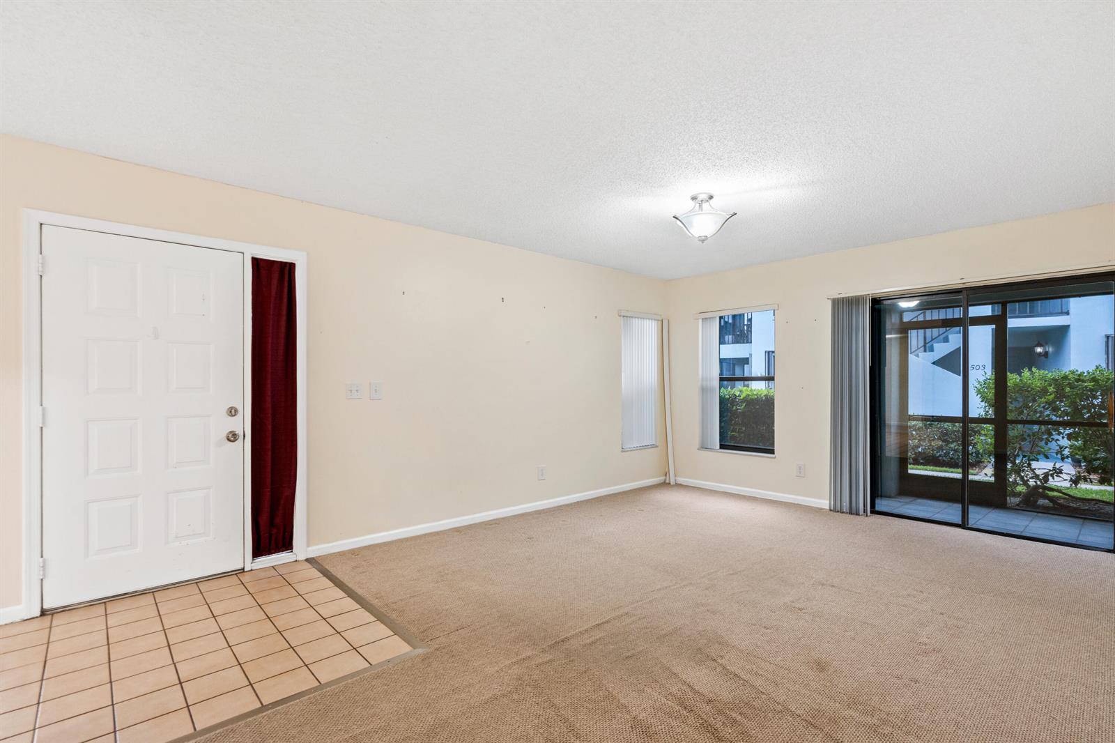 An empty living room features beige carpet, tile flooring by the door, and sliding glass doors — 950 S Kanner Highway # 402, Stuart FL 34994, STUART, FL